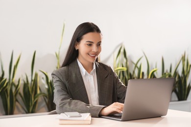 Happy woman using modern laptop at desk in office