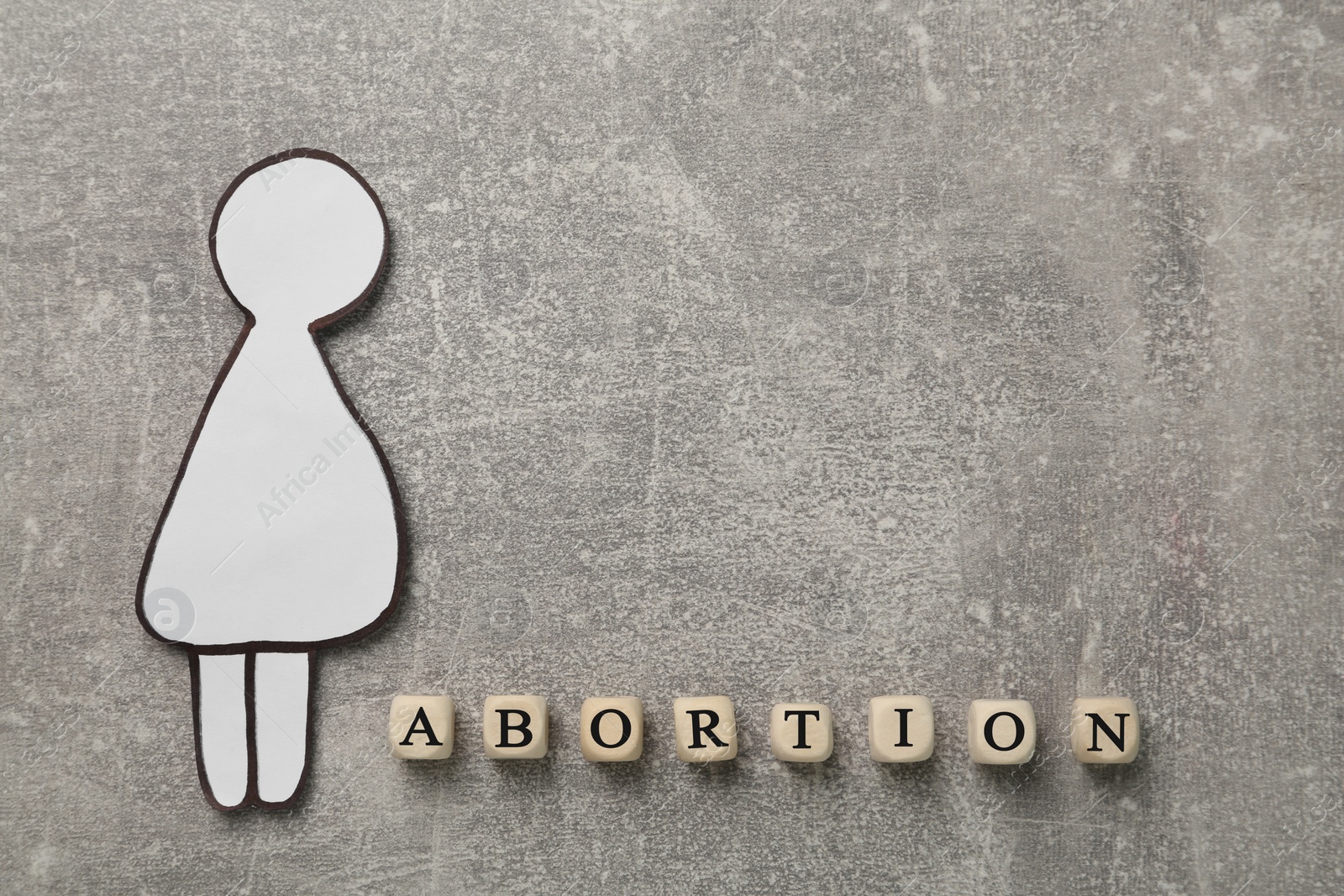 Photo of Word Abortion made of wooden cubes and pregnant woman paper cutout on grey background, flat lay. Space for text