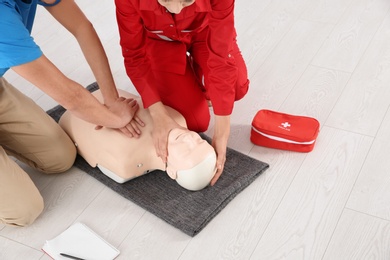 Photo of Instructor and man practicing first aid on mannequin indoors, closeup