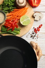 Flat lay composition with black wok and products on light wooden table