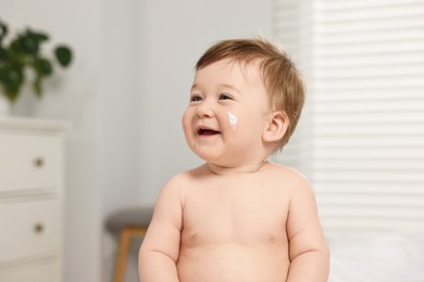 Photo of Cute little baby with moisturizing cream on face indoors