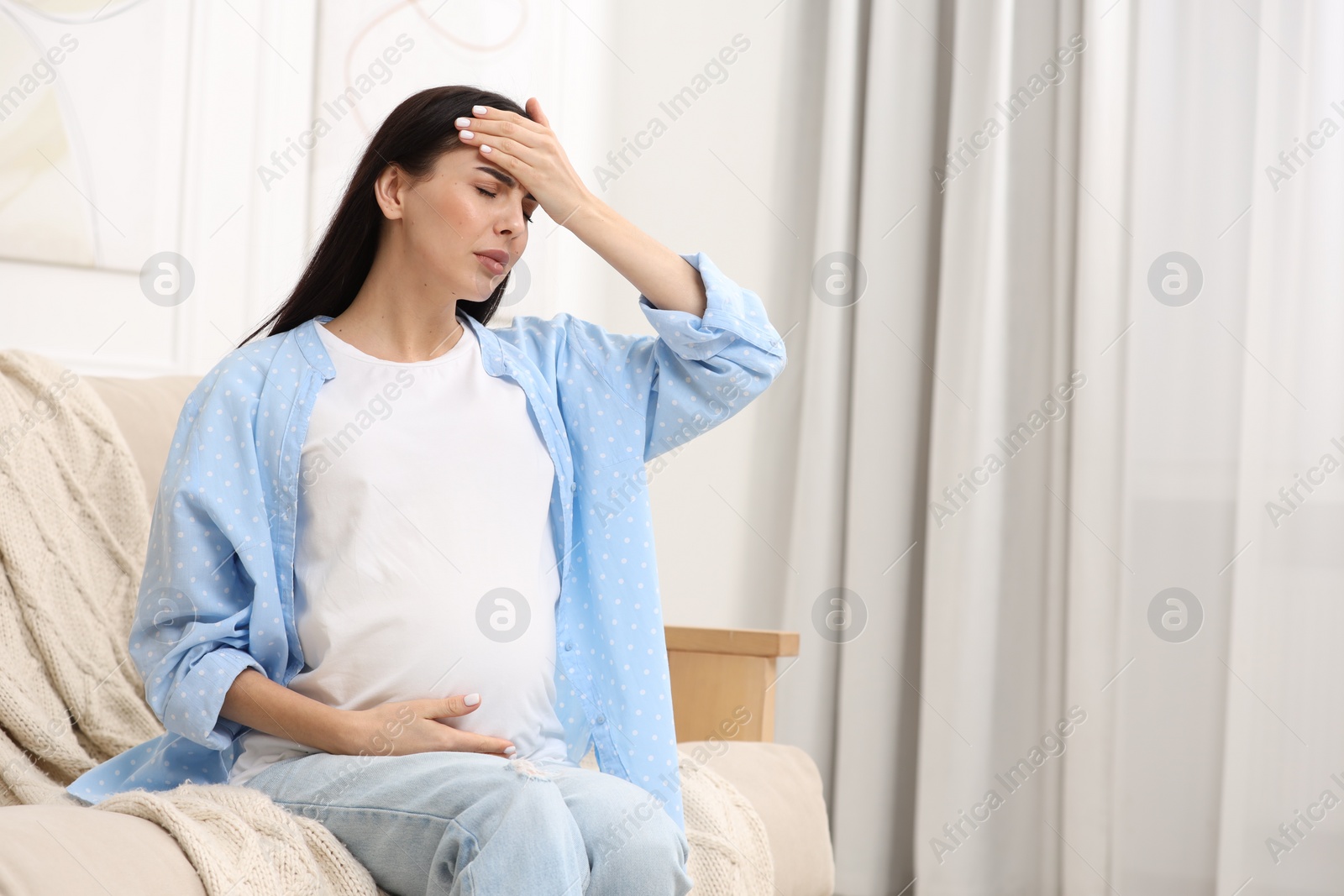 Photo of Pregnant woman suffering from headache on sofa at home, space for text