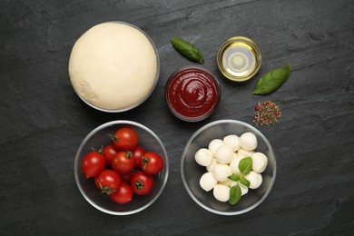 Photo of Raw dough and other ingredients for pizza on black table, flat lay