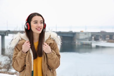 Photo of Beautiful young woman listening to music with headphones outdoors. Space for text