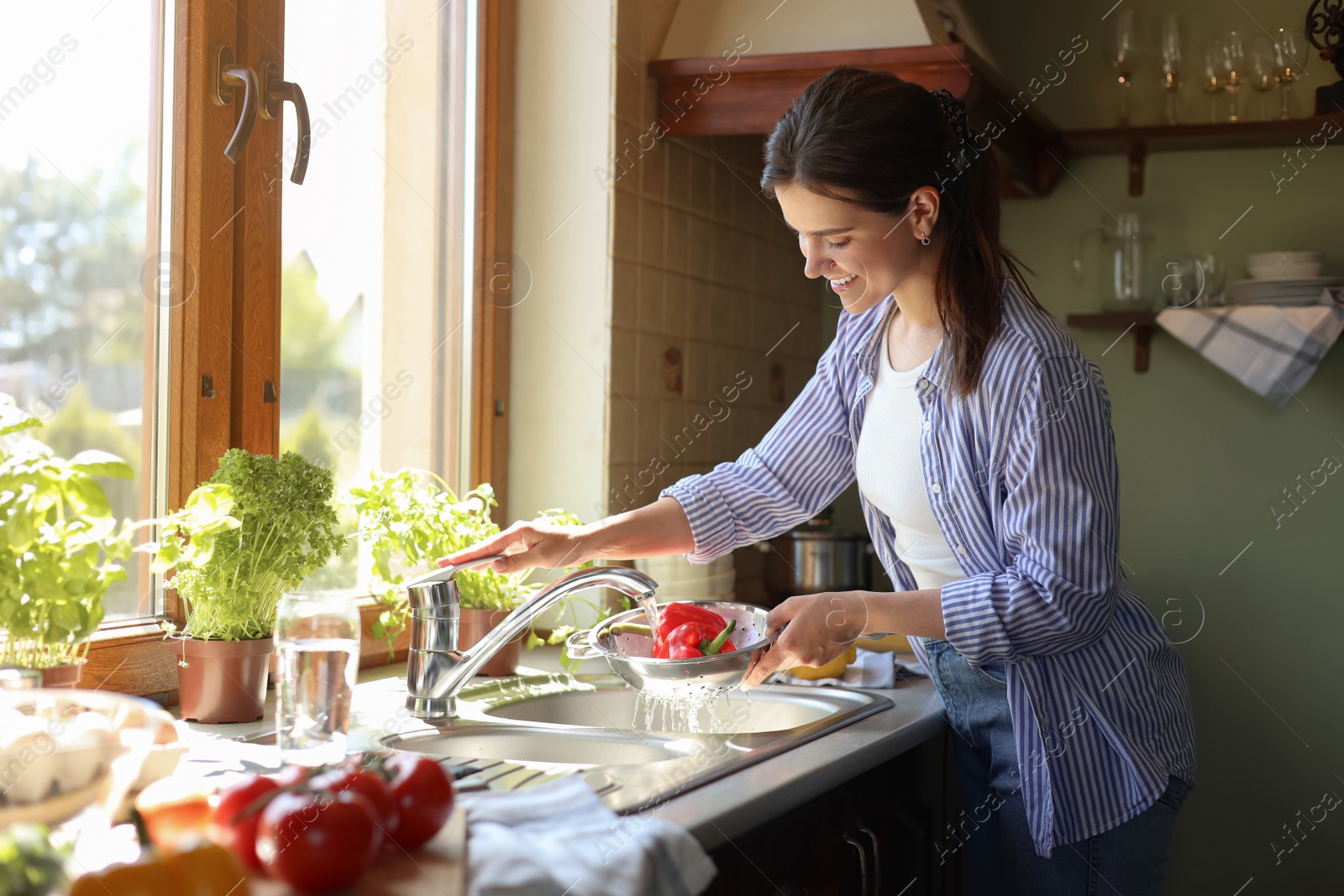 Photo of Young woman washing fresh bell peppers in kitchen sink