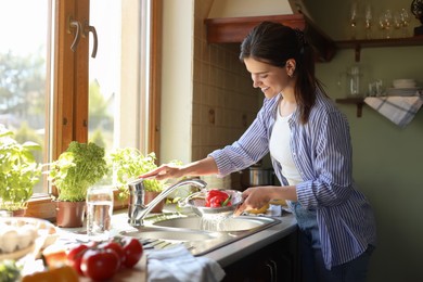 Young woman washing fresh bell peppers in kitchen sink