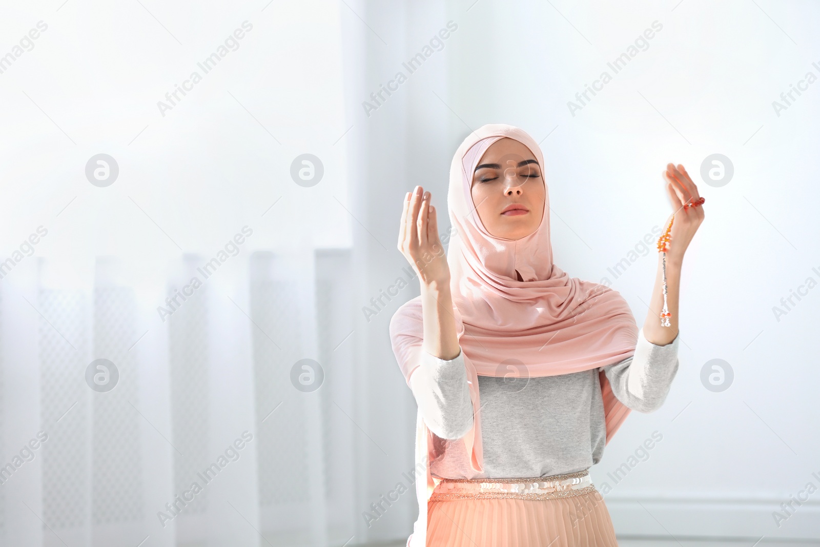 Photo of Young Muslim woman in hijab praying indoors. Space for text