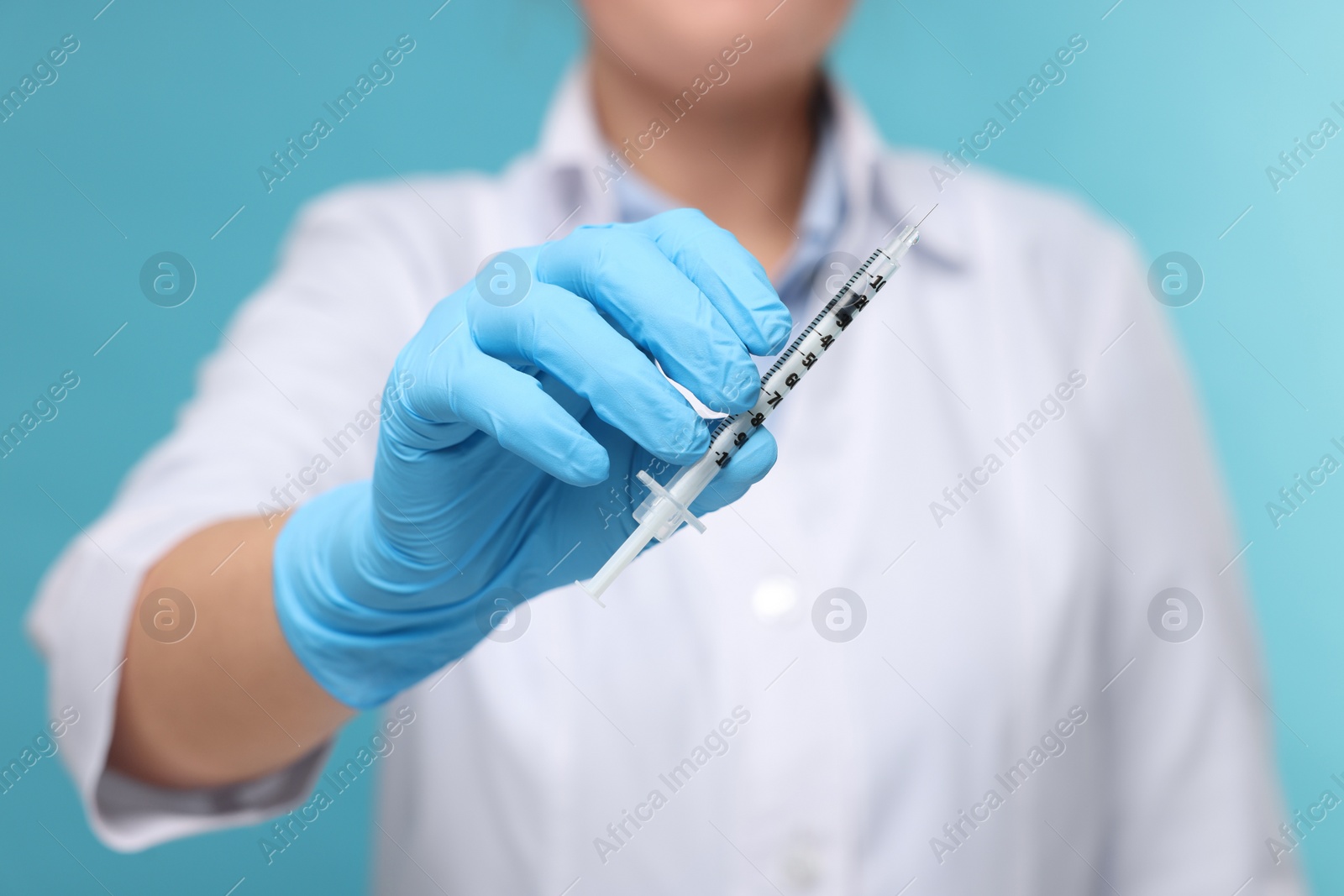 Photo of Doctor holding syringe on light blue background, closeup