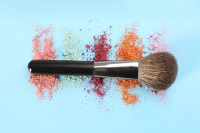 Makeup brush and scattered eye shadows on light blue background, flat lay