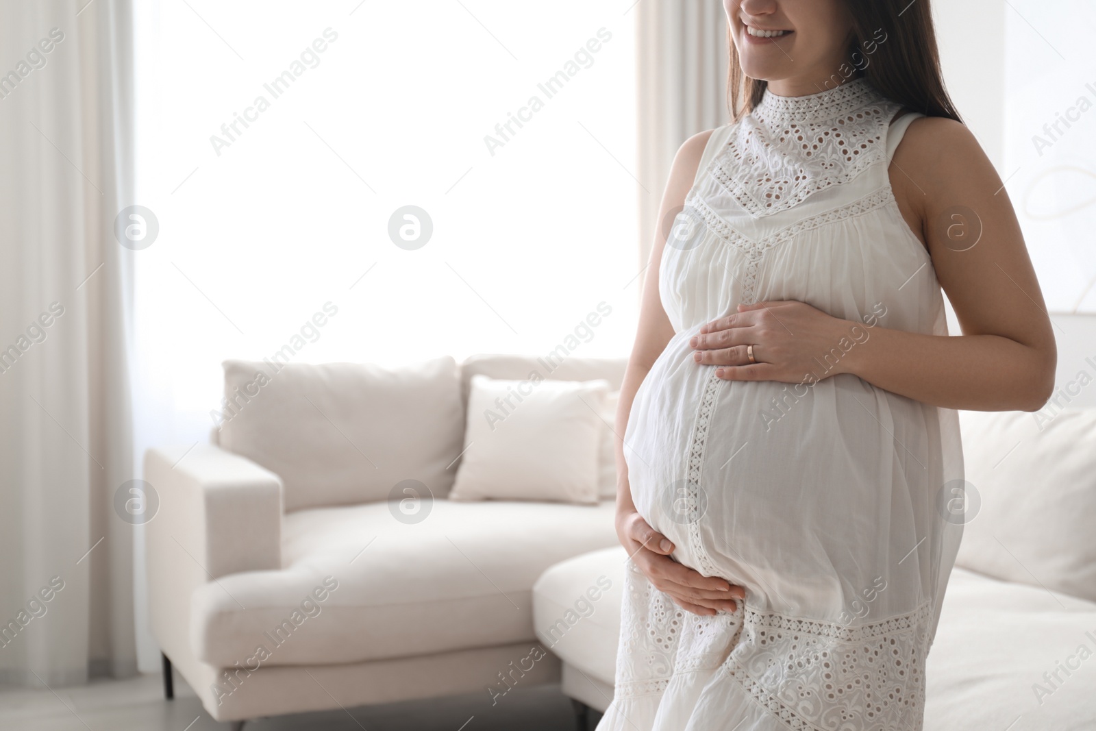 Photo of Pregnant young woman touching belly at home, closeup. Space for text