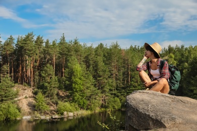 Photo of Young woman on rock near lake and forest. Camping season