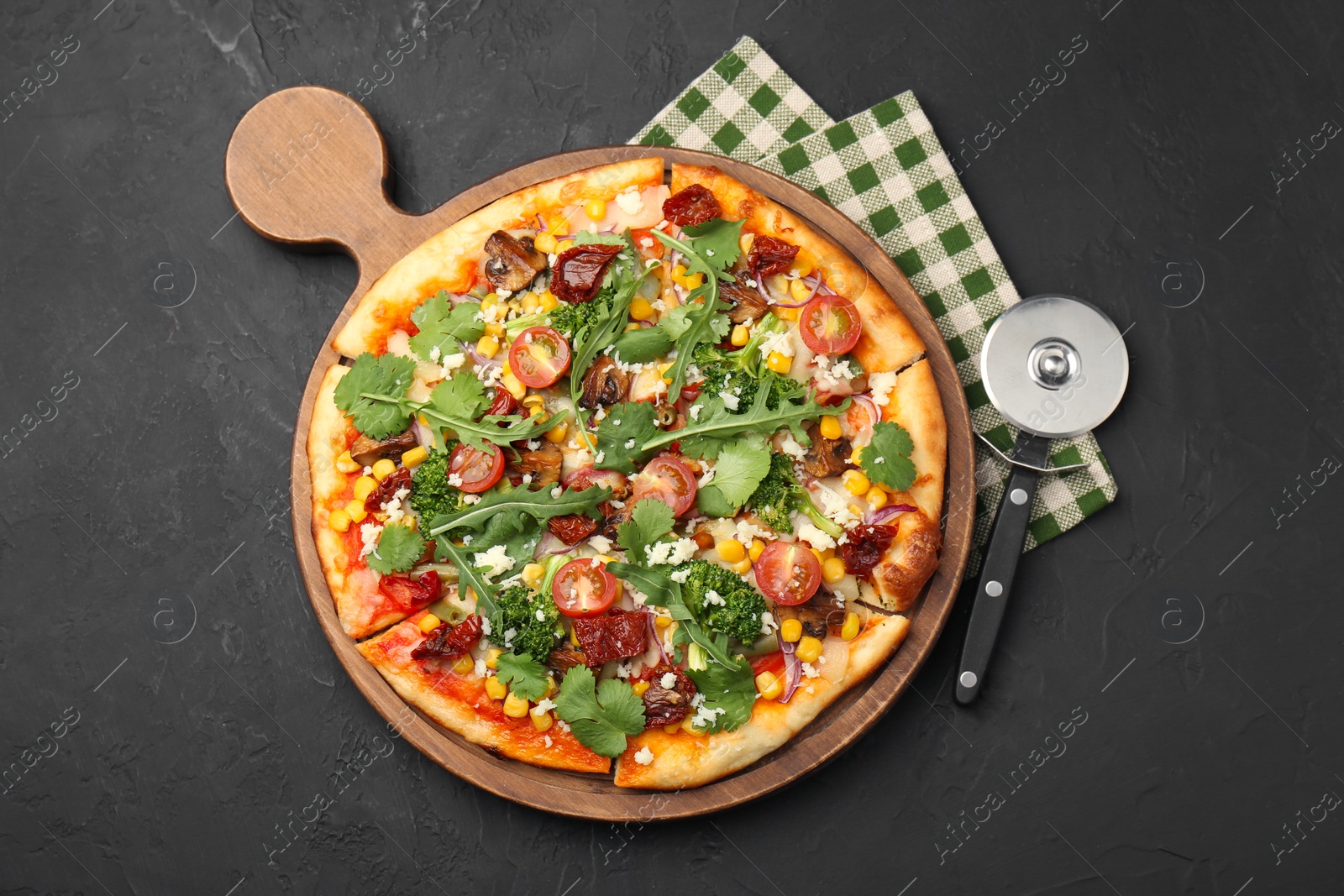 Photo of Delicious vegetarian pizza and cutter on black table, top view