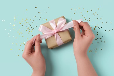 Photo of Woman with gift box and confetti on light blue background, top view