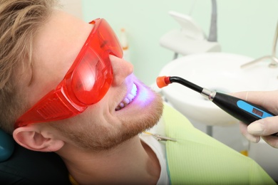 Photo of Young patient undergoing teeth whitening procedure in clinic. Visit dentist