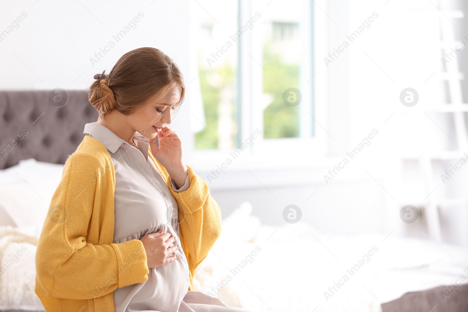 Photo of Happy pregnant woman sitting in bedroom at home