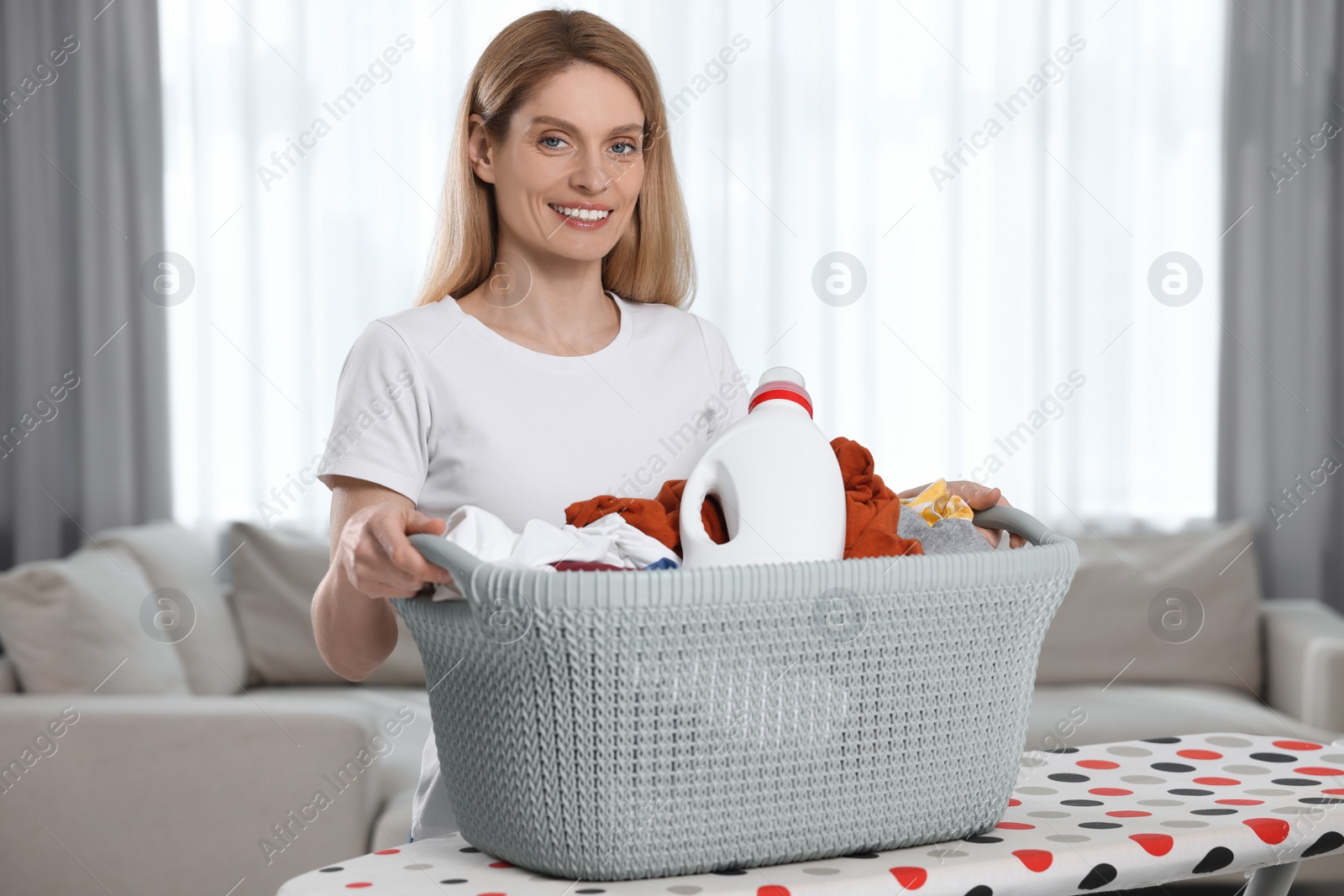 Photo of Woman holding basket with dirty clothes and fabric softener in room