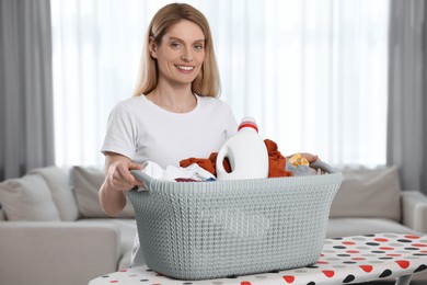 Woman holding basket with dirty clothes and fabric softener in room