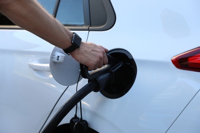 Photo of Man inserting plug into electric car socket at charging station, closeup
