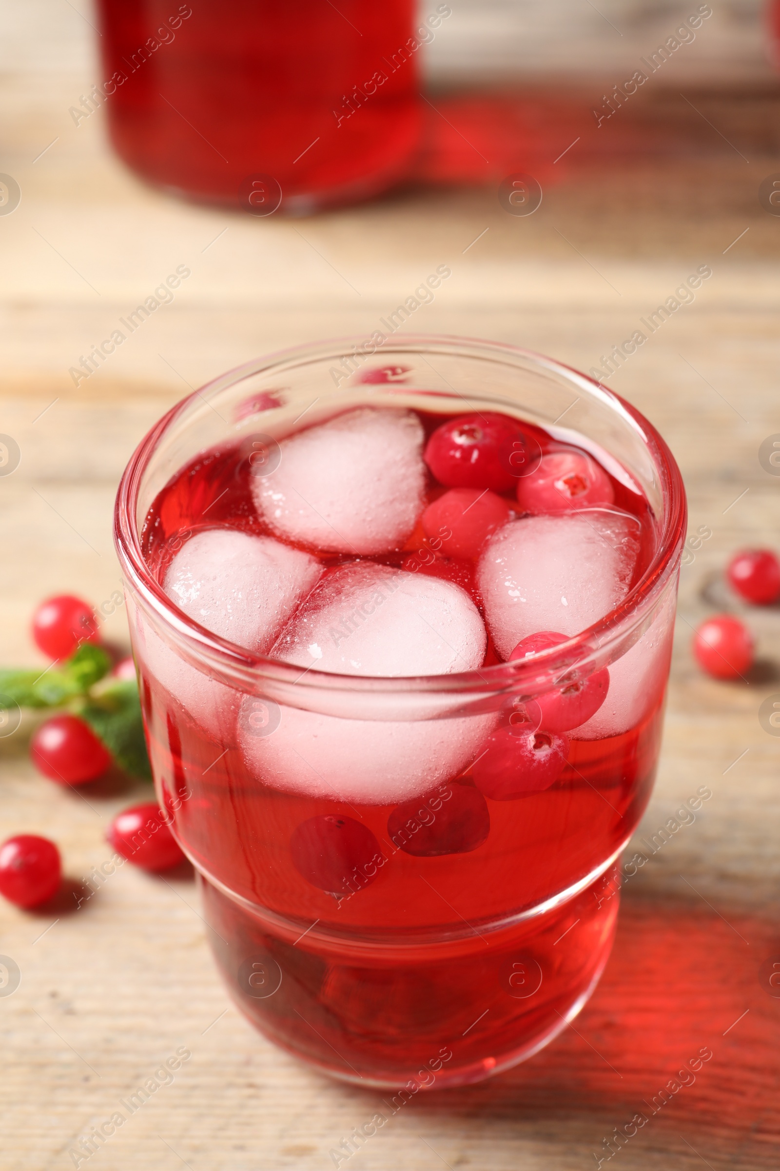 Photo of Tasty cranberry juice with ice cubes in glass and fresh berries on wooden table, closeup