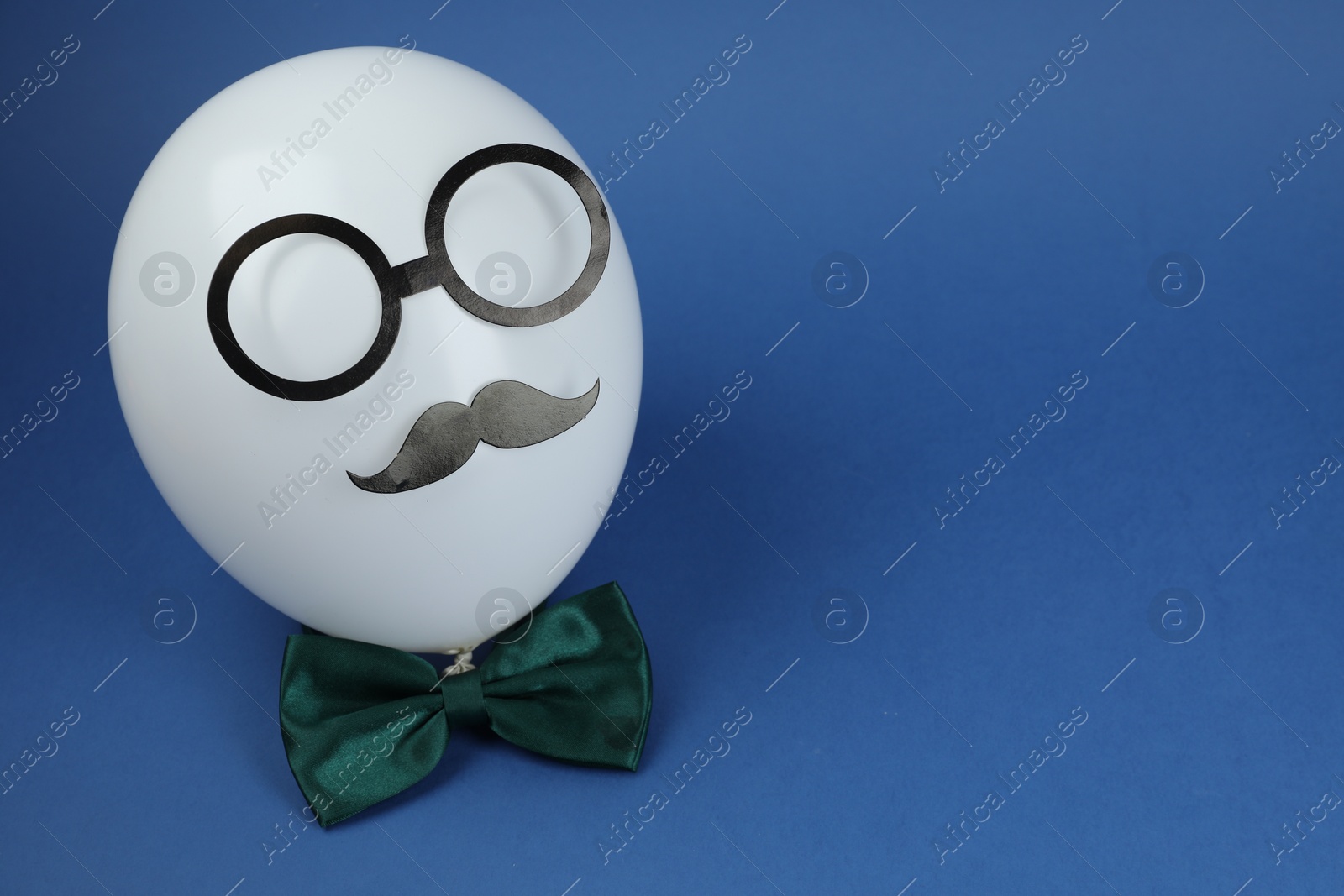 Photo of Man's face made of balloon, fake mustache, paper glasses and bow tie on blue background. Space for text