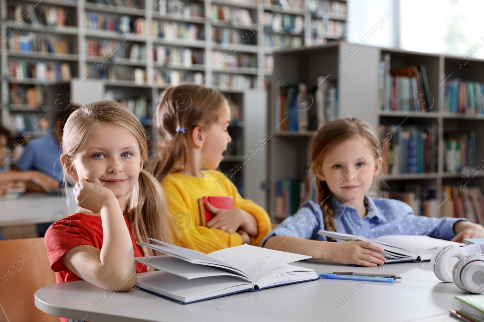 Photo of Happy little girls reading books at table in library