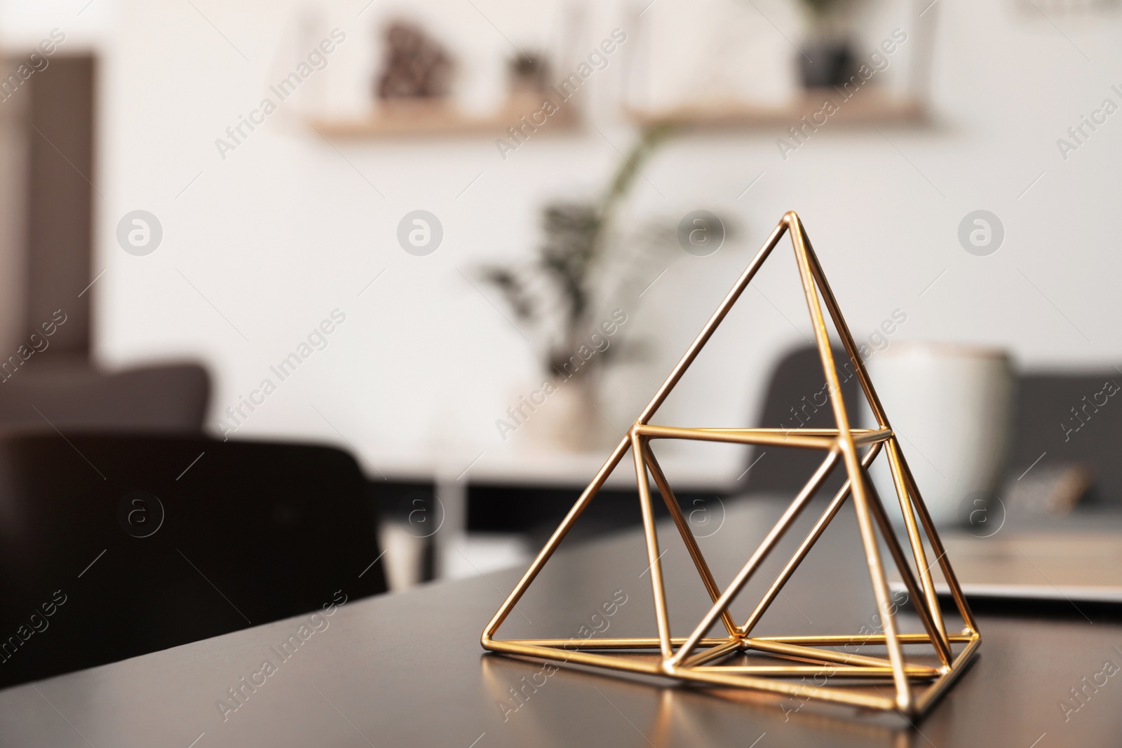 Photo of Decorative metal pyramid on table in room. Modern interior element