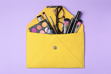 Photo of Cosmetic bag with makeup products and beauty accessories on violet background, top view