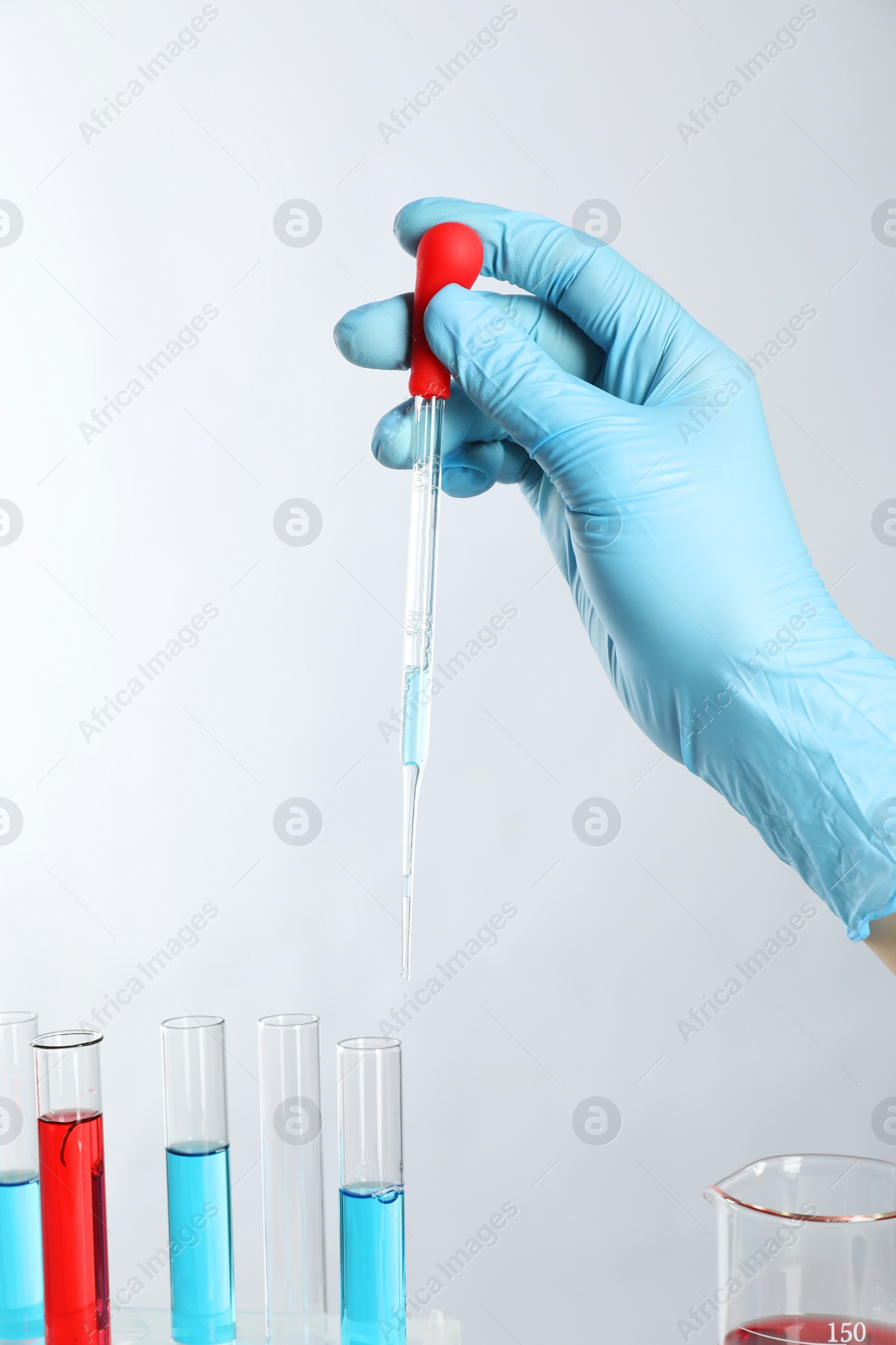 Photo of Scientist dripping liquid from pipette into test tube on light background, closeup