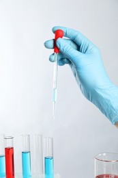 Photo of Scientist dripping liquid from pipette into test tube on light background, closeup