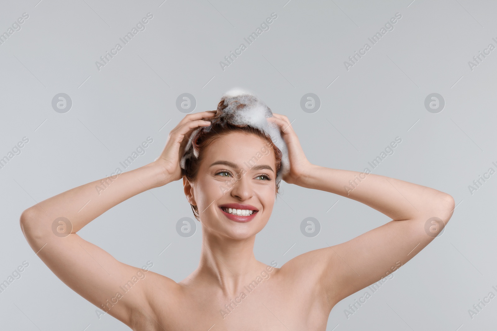 Photo of Happy young woman washing her hair with shampoo on light grey background