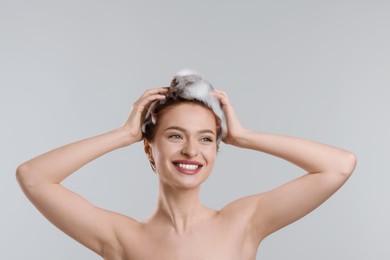 Happy young woman washing her hair with shampoo on light grey background