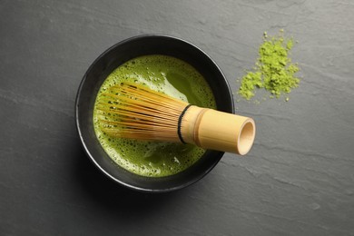 Photo of Cup of fresh matcha tea with bamboo whisk on black table, flat lay