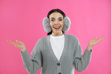 Beautiful young woman wearing earmuffs on pink background