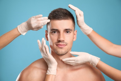 Photo of Doctors examining man's face for cosmetic surgery on light blue background