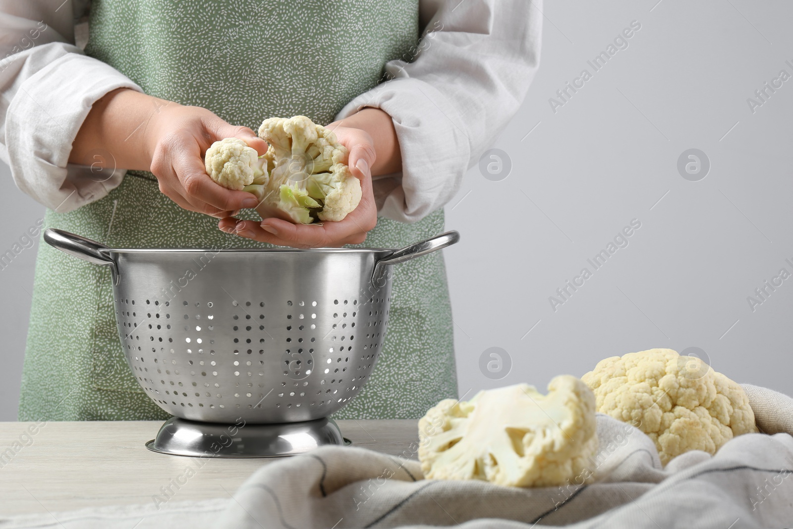 Photo of Woman separating fresh cauliflower cabbage above colander at wooden table, closeup