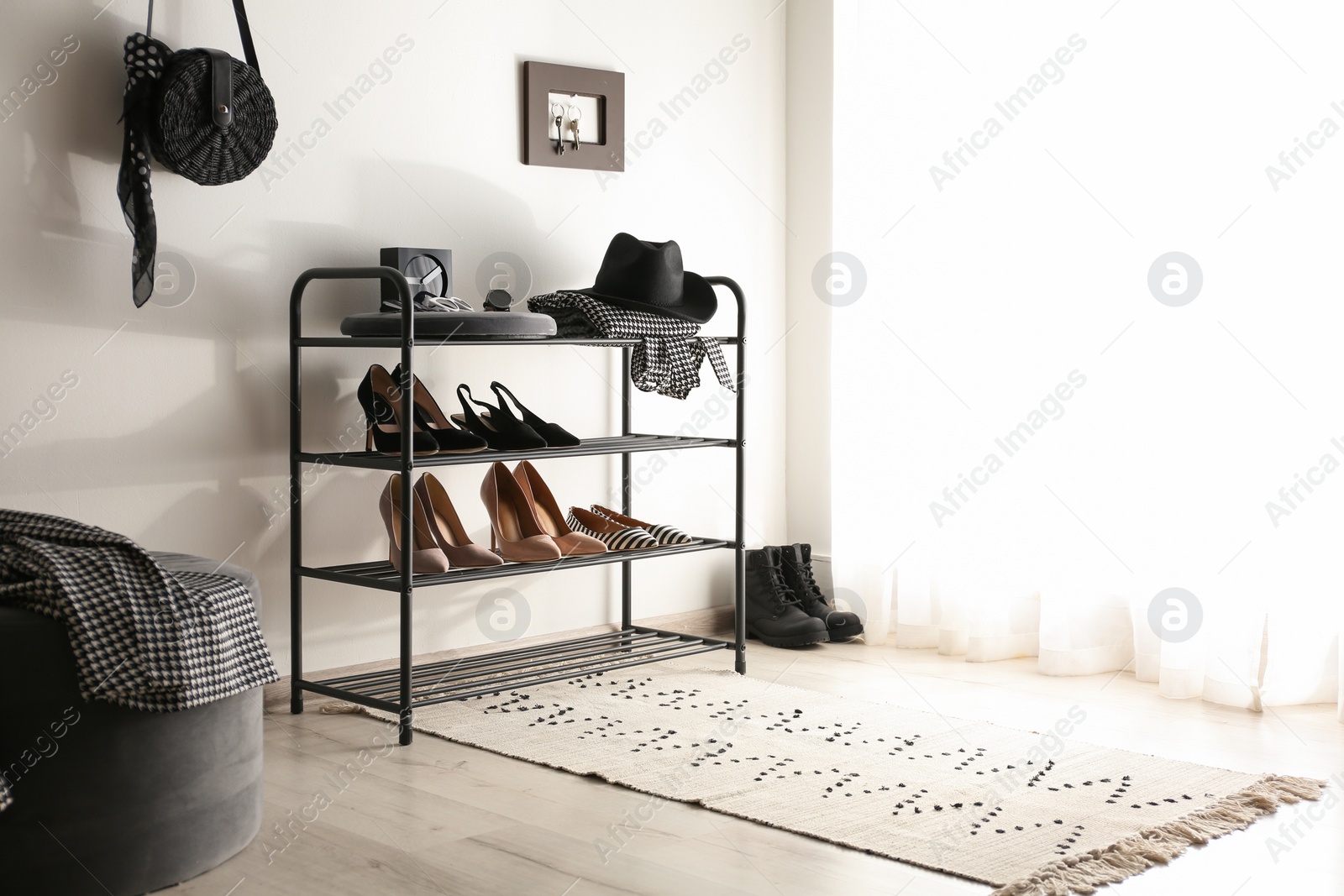 Photo of Black shelving unit with shoes and different accessories near white wall. Space for text