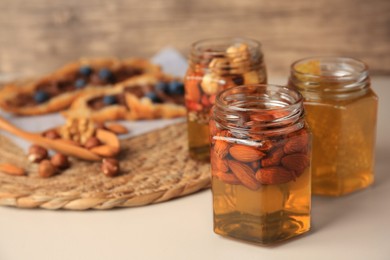 Photo of Jars with nuts and honey on beige table, space for text