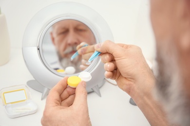 Photo of Senior man taking contact lens from container in front of mirror