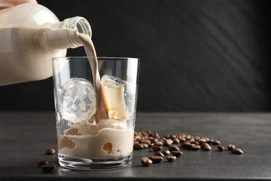 Pouring coffee cream liqueur into glass at grey table, closeup. Space for text