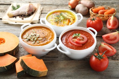 Photo of Tasty broth, cream soups in bowls and ingredients on old wooden table