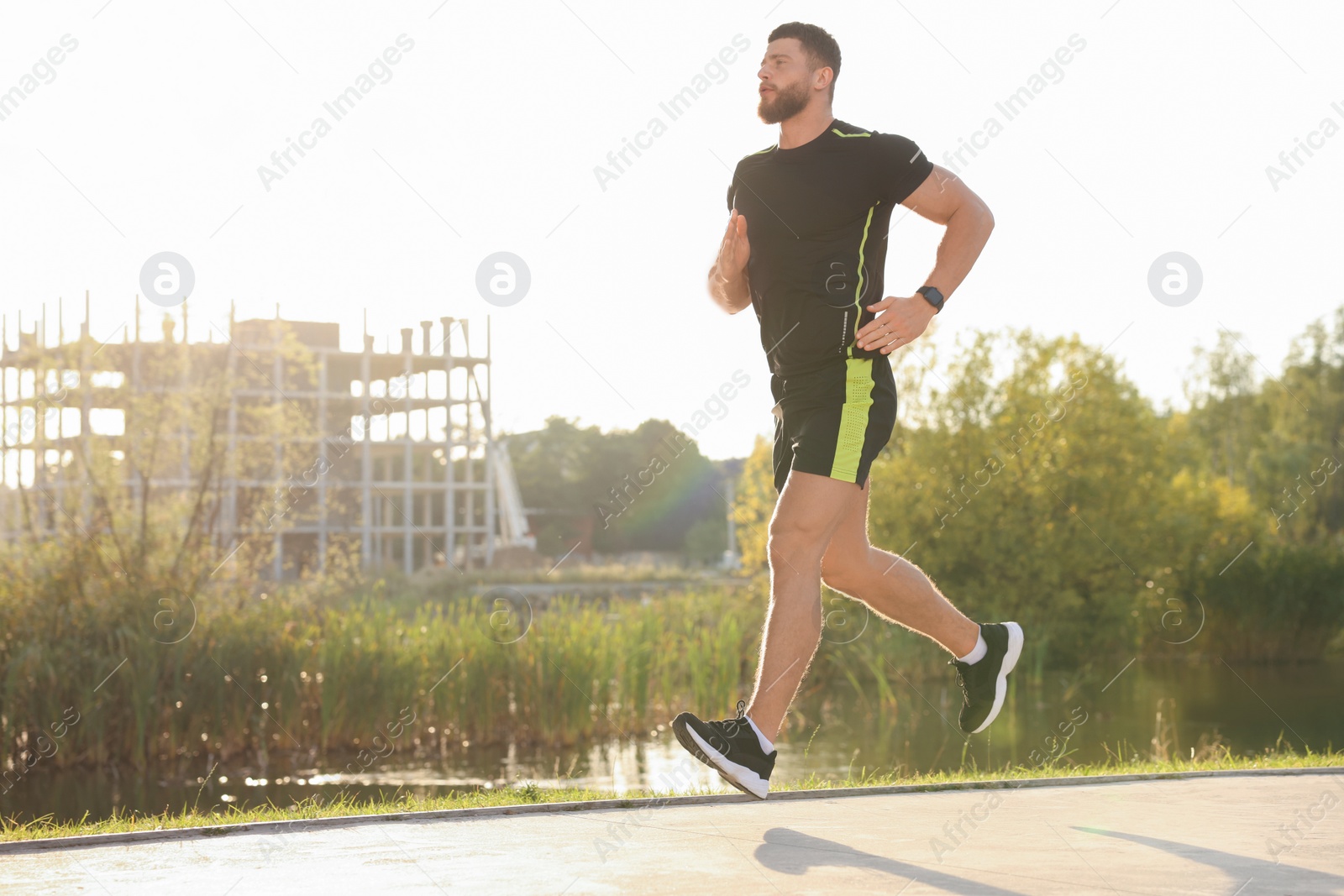 Photo of Young man running near pond in park. Space for text