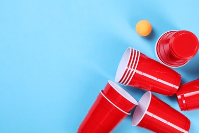 Photo of Plastic cups and ball on light blue background, flat lay with space for text. Beer pong game