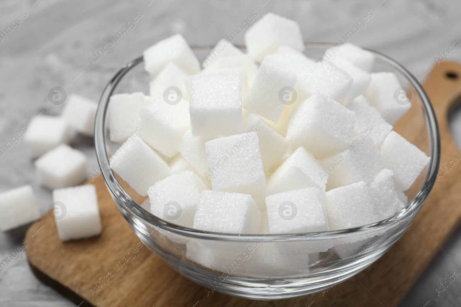 Photo of White sugar cubes in glass bowl on grey table, closeup