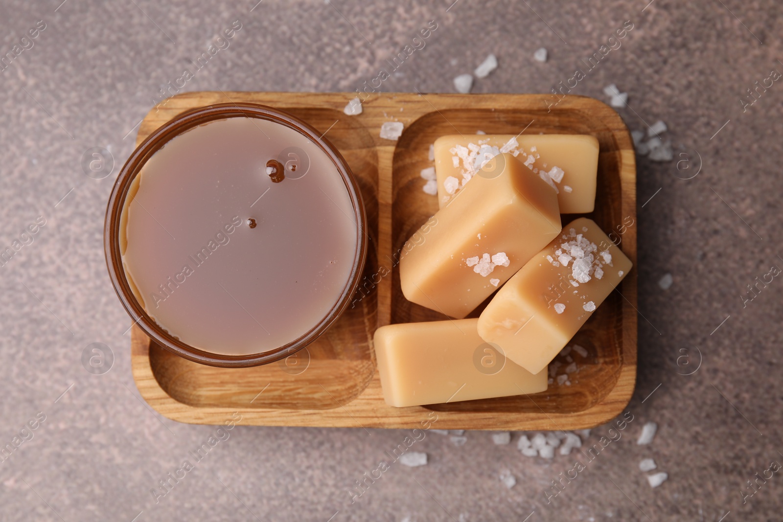 Photo of Yummy caramel candies, sauce and sea salt on brown table, top view