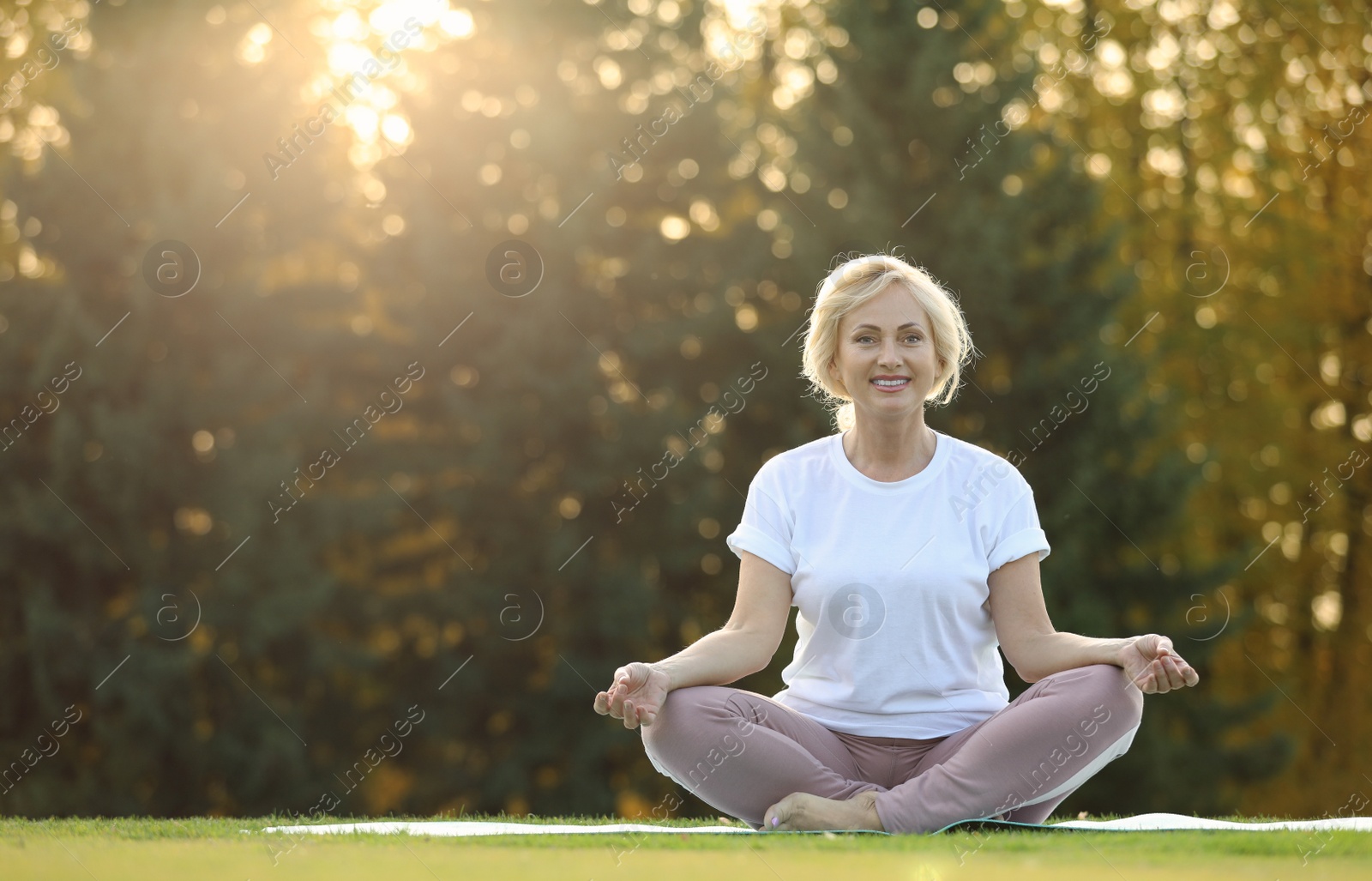 Image of Mature woman practicing yoga on green grass in park