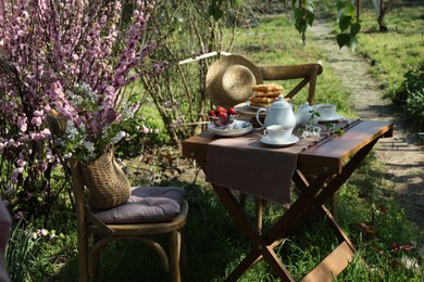 Photo of Beautiful spring flowers, freshly baked waffles and ripe strawberries on table served for tea drinking in garden