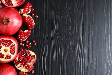 Photo of Ripe pomegranates on dark wooden background, top view with space for text