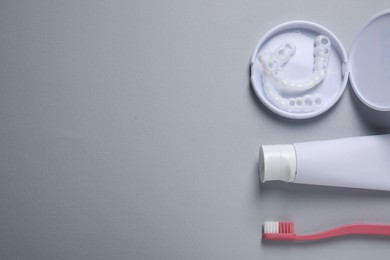 Bite correction. Toothpaste, brush and dental mouth guards on grey background, flat lay. Space for text
