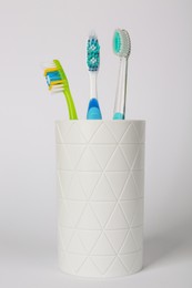 Photo of Different toothbrushes in holder on light grey background