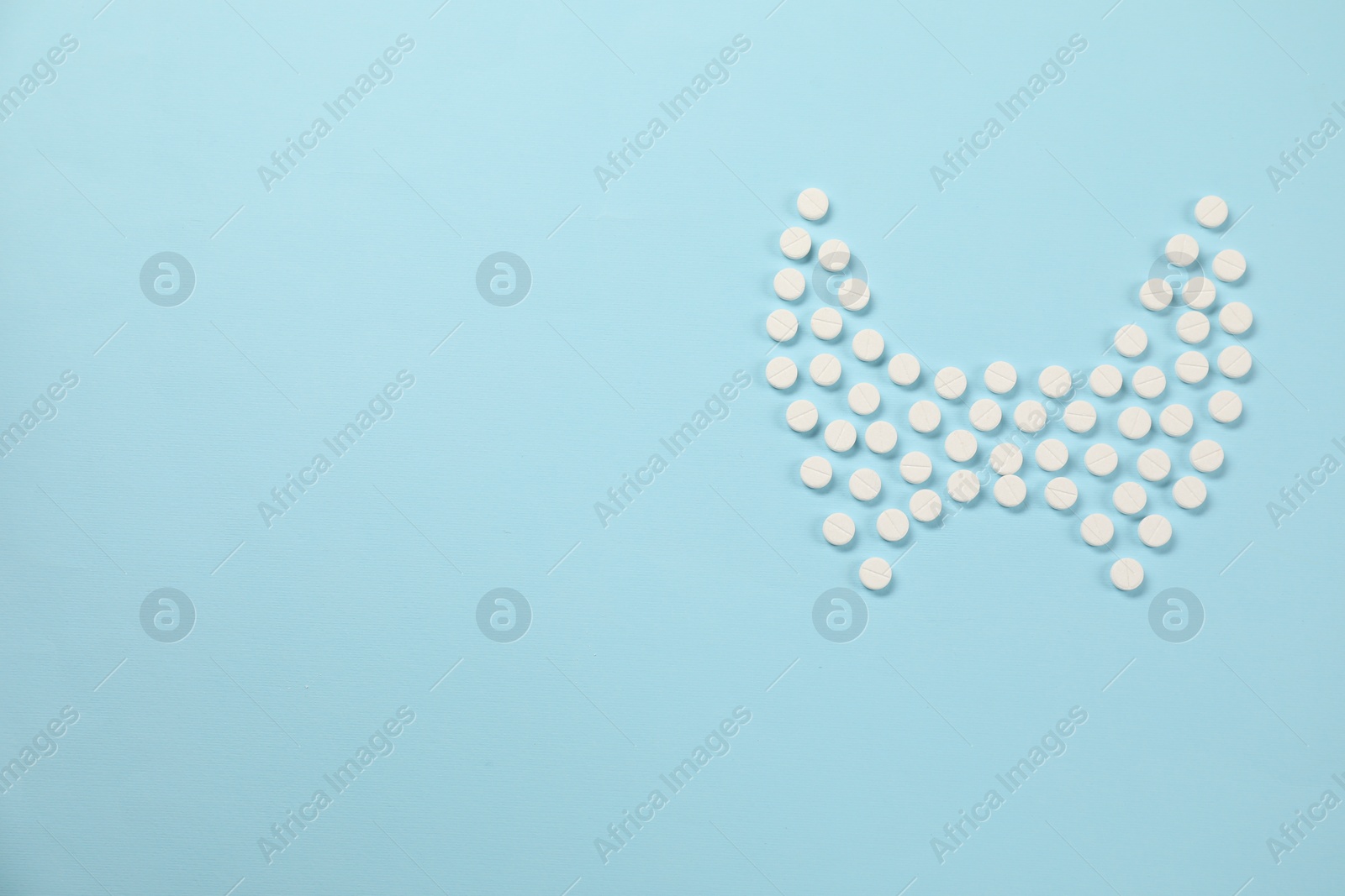 Photo of Endocrinology, Shape of thyroid gland made of pills on light blue background, flat lay. Space for text